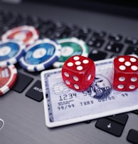 A set of red dice and poker chips are placed on top of a credit card, which is situated on a laptop keyboard. The poker chips are in various colors, including blue, green, red, and white.