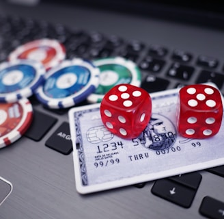 A set of red dice and poker chips are placed on top of a credit card, which is situated on a laptop keyboard. The poker chips are in various colors, including blue, green, red, and white.
